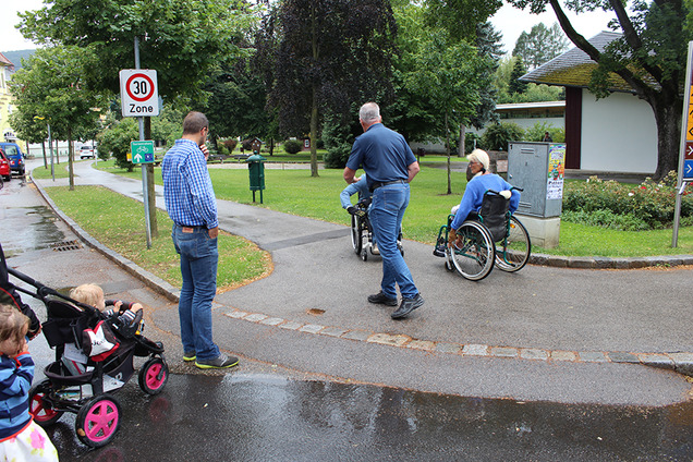 Teilnehmende einer Gemeindebegehung im Rollstuhl und mit Kinderwagen überqueren eine Straße