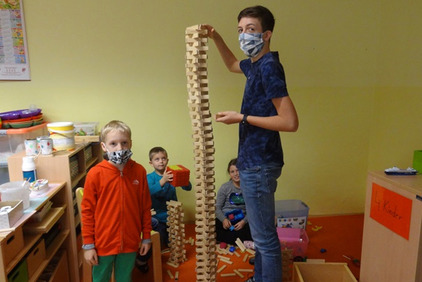 Ein Betreuer und ein paar Kinder bauen einen hohen Turm aus Holzstücken.