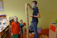 Ein Betreuer und ein paar Kinder bauen einen hohen Turm aus Holzstücken.