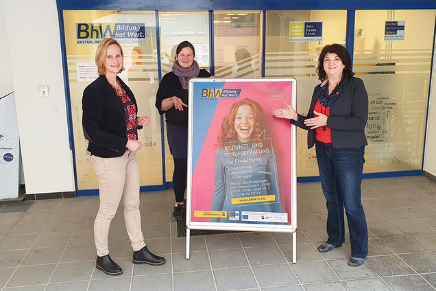 Gruppenbild mit den genannten drei Personen. Sie stehen vor der Tür des offenen Beratungsraums. Zwischen ihnen steht ein großer A-Ständer mit einem Plakat des offenen Beratungsraums.
