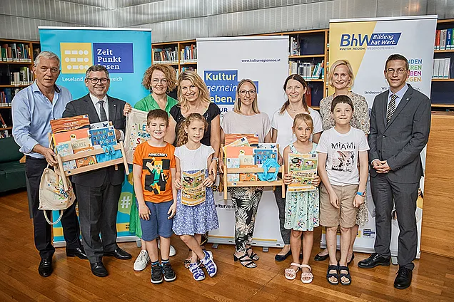 Auf einem Gruppenbild lächeln die Gewinnerkinder des Lesepasses mit ihren Lehrerinnen und Direktorinnen in die Kamera. Sie haben Bücherpakete und Lesesackerl in den Händen. 