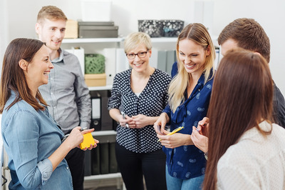 Eine Gruppe junger Frauen und Männer steht in einem Büro zusammen und besprechen etwas.