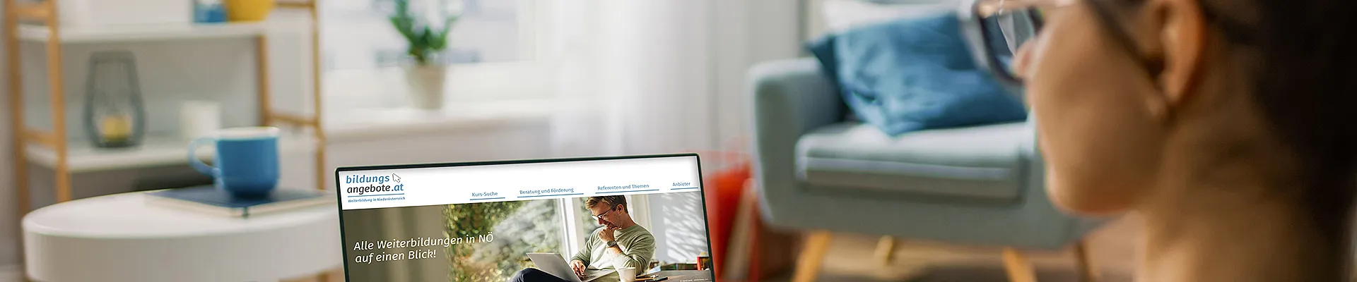 Eine Frau sitzt auf der Couch, hat einen Laptop am Schoss und schaut in die Bildungsdatenbank NÖ.