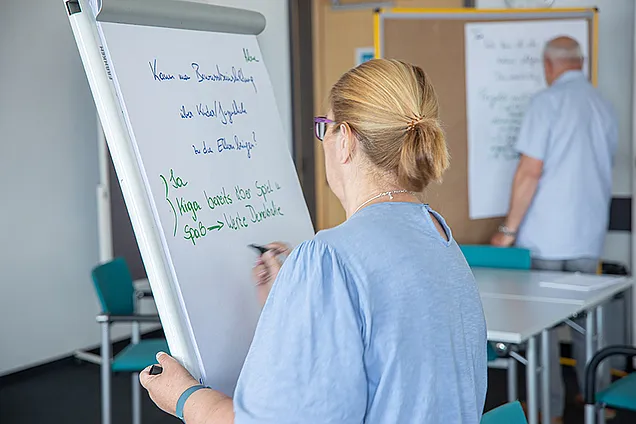 Eine ehrenamtliche BHW Leiterin steht vor einem Flipchart und notiert mit einemm grünen Stift einige Stichpunkte.