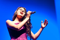 Ein dunkelhaariges Mädchen im violetten Kleid singt voller Inbrunst in ein Mikrofon.