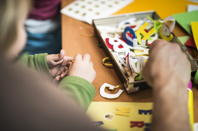 Nahaufnahme von Kinder- und Erwachsnenehänden die in einer Schachtel mit Spielzeug-Buchstaben wühlen.