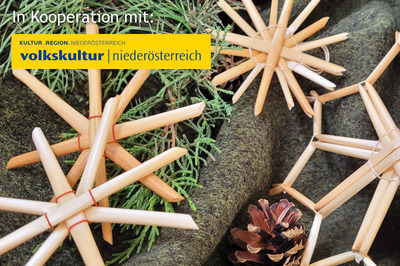 Strohsterne liegend auf einem grauen Hintergrund. Daneben liegen ein paar grüne Zweige und ein kleiner Tannenzapfen.