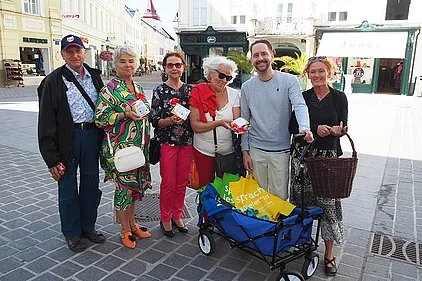 Schauspieler Sven Kaschte und Basisbildungs-Trainerinnen Brigitte Schönsleben-Thiery und Ottilie Roll verteilen Buchstabennudeln-Sackerl. Daran befestigt: QR-Codes, die zu Lesetipps für die Familie auf der BhW-Website führen.