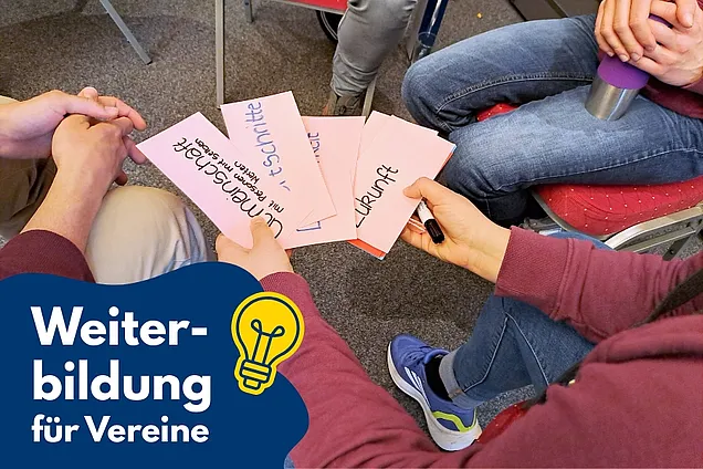Auf dem Bild sitzen mehrere Personen zusammen und halten beschriftete Karten in den Händen, auf denen Begriffe wie „Zukunft“ und „Umgestaltung“ stehen. Rechts unten ist ein grafisches Element mit der Aufschrift „Weiterbildung für Vereine“ und kleinen Glühbirnen-Symbolen zu sehen.
