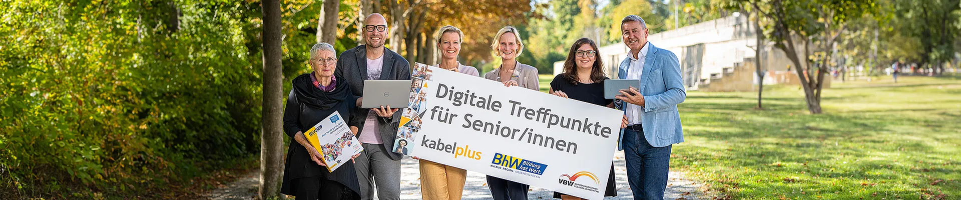 Kursteilnehmerin Hermine Schlag, Trainer Hannes Giefing, Geschäftsführerin des Burgenländischen Volksbildungswerks Judith Tscheppe, BhW Geschäftsführerin Therese Reinel, Trainerin Julia Hentschel und kabelplus Geschäftsführer Wolfgang Schäffer stehen in einer Reihe und halten ein Schild „Digitale Treffpunkte für Senior/innen“ in die Kamera. 
