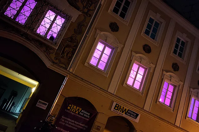 Die Fassade des BhW Gebäudes bei Nacht mit lila erleuchteten Fenstern und violetten Bannern