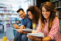 Ein junger Mann und zwei junge Frauen sitzen in einer Bibliothek und lesen in ihren Skripten.