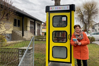 Das Foto zeigt Bildungsgemeinderätin Roswitha Ronge neben einer ihrer umgestalteten Telefonzellen. Sie hält ein Buch im Arm.