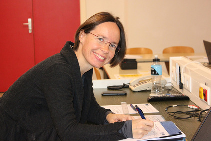 Die Lernbegleiterin Renate Ömer ist gerade dabei etwas auf einen Zettel zu schreiben, aber für das Foto dreht sie ihren Kopf in die Kamera und lacht.