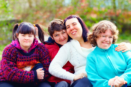 Eine Gruppe junger Frauen mit Down-Syndrom sitzen hintereinander in der Natur und lachen in die Kamera