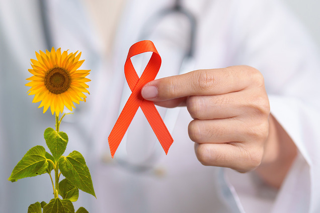 Eine Frauenhand hält eine orangefarbene Schleife als Symbol der Solidarität mit Multiple-Sklerose-Betroffenen
