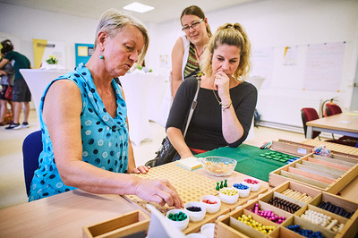 Eine Teilnehmerin der Basisbildung hört gespannt einer Lernbegleiterin zu. Eine zweite Teilnehmerin schaut interessiert über die Schulter