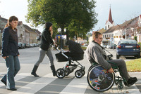 Mehrere Menschen überqueren einen Zebrastreifen, zwei Frauen, eine davon mit Kinderwagen und ein Mann im Rollstul