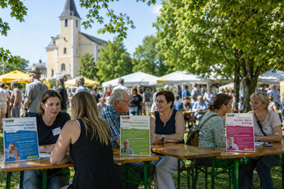 Personen sitzen bei einem Gemeindefest an Tischen. Man sieht Schilder mit Gesprächs-Inputs. Alle unterhalten sich.