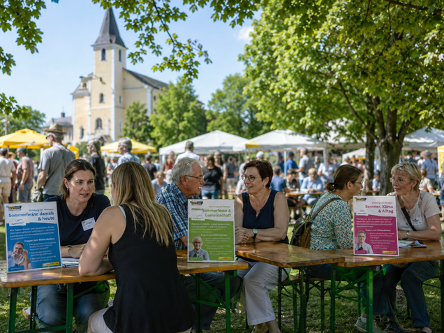 Personen sitzen bei einem Gemeindefest an Tischen. Man sieht Schilder mit Gesprächs-Inputs. Alle unterhalten sich.