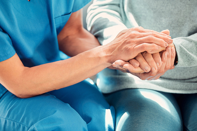 Die Hände einer Person in Pflegeberufs-Kleidung halten die Hände einer anderen Person, die wahrscheinlich von ihr betreut wird.