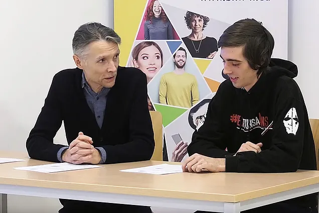 Lernbegleiter Michael und Teilnehmer Matthias sitzen an einem Tisch und schauen auf Lernunterlagen.