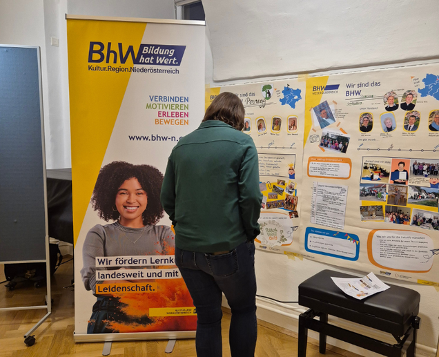 Es wird der Empfangsbereich gezeigt mit einem Rollup von dem BhW Niederösterreich und einer Info Wand. Eine Person steht davor und sieht sich alles an.