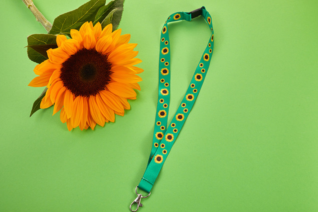 Eine Sonnenblume und ein grünes Schlüsselband mit Sonnenblumen-Aufdruck als Symbol für nicht sichtbare Behinderungen