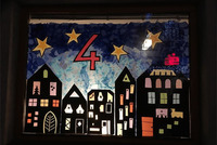Das Bild zeigt ein Adventfenster. Aus schwarzer Pappe gebastelt wurde eine Wohnhaussiedlung bei Nacht. Alle Fenster sind bunt beleuchtet. Am Sternenhimmel ist die Adventfensternummer 4 zu lesen.
