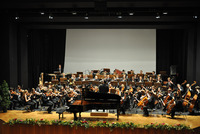 Ein Jugendorchester spielt ein Konzert in einem Konzertsaal. In der Mitte ist ein schwarzer Klavierflügel zu sehen.