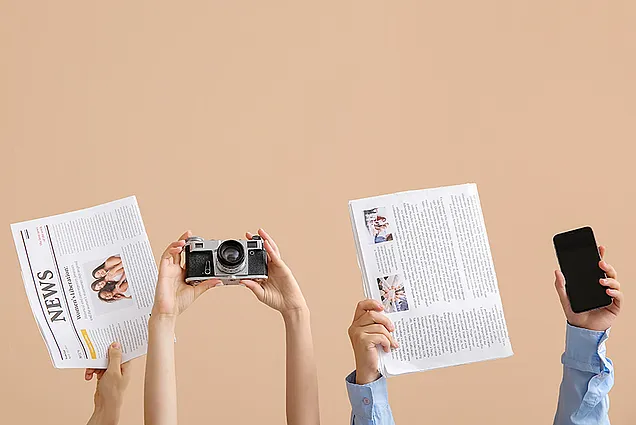 Das Bild zeigt einige hochgestreckte Arme, die Zeitungen, eine Kamera und ein Smartphone halten.