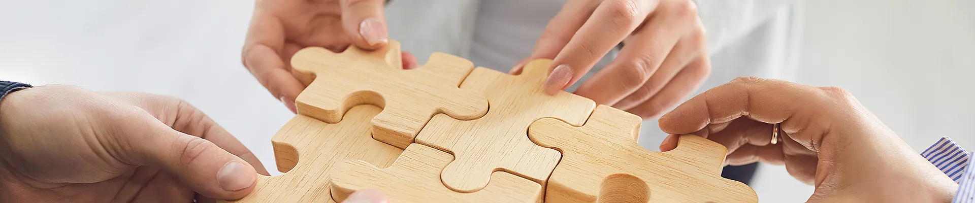 Das Bild die Hände mehrerer Personen, die gemeinsam Puzzle-Teile aus Holz zusammenfügen.