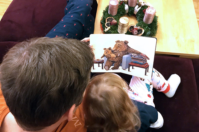 Zwei Kinder sitzen auf der Couch und schauen sich ein Kinderbuch an. Man ieh tnur ihre beiden Kinderköpfe und das vor ihnen aufgeschlagene Buch.