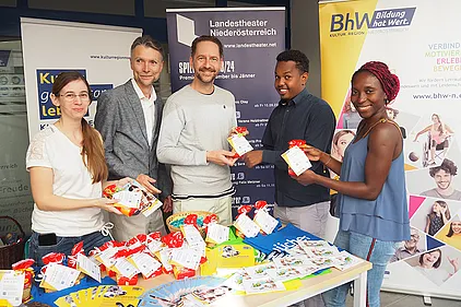 Stellvertretender Projektleiter und Lernbegleiter der  Basisbildung NÖ Michael Lindenhofer, Basisbildungs-Mitarbeiterin Claudia Geist und Schauspieler Sven Kaschte und zwei Passenten. Sie halten kleine Sackerl mit Buchstaben-Nudeln und einem Info-Zettel über den Weltalphabetisierungstag in den Händen.