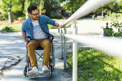 Ein Mann im Rollstuhl hält sich an einem Geländer fest um eine Rampe hoch zu kommen.