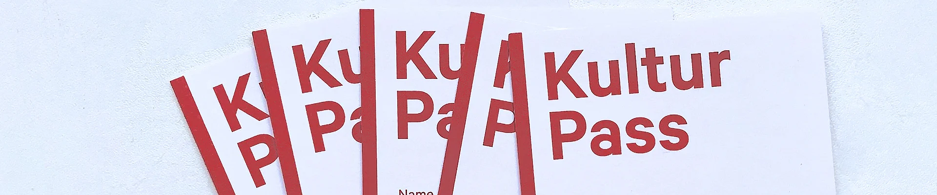 Foto von mehreren Kulturpässen. Es steht auf einem ca. A7 großen Karton, in roter Schrift, Kulturpass, dann Felder zum Ausfüllen für Name und Geburtsdatum. Und man sieht das Logo: das besteht aus einem roten Männchen mit Messer und Gabel in der Hand und daneben steht: Hunger auf Kunst & Kultur