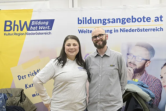Stefanie Halbwachs (bildungsangebote.at) und Tobias Hauzeneder (BhW Basisbildung) vorm Stand des BhW auf dem Tag der Weiterbildung in der AK NÖ.