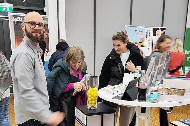 Im Vordergrund steht Tobias Hauzeneder (BhW Basisbildung). Im Hintergrund stehen interessierte Damen und schauen sich Infomaterial an.
