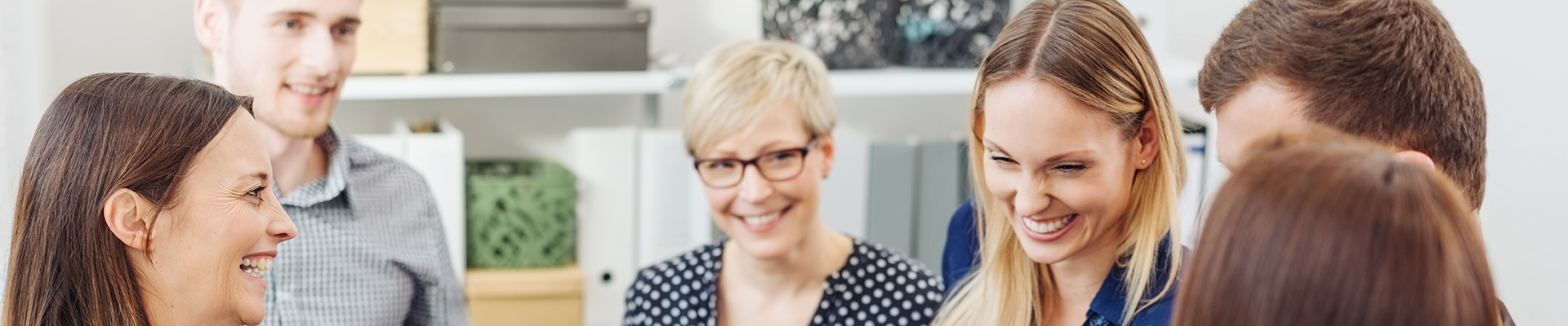 Eine Gruppe junger Frauen und Männer steht in einem Büro zusammen und besprechen etwas.