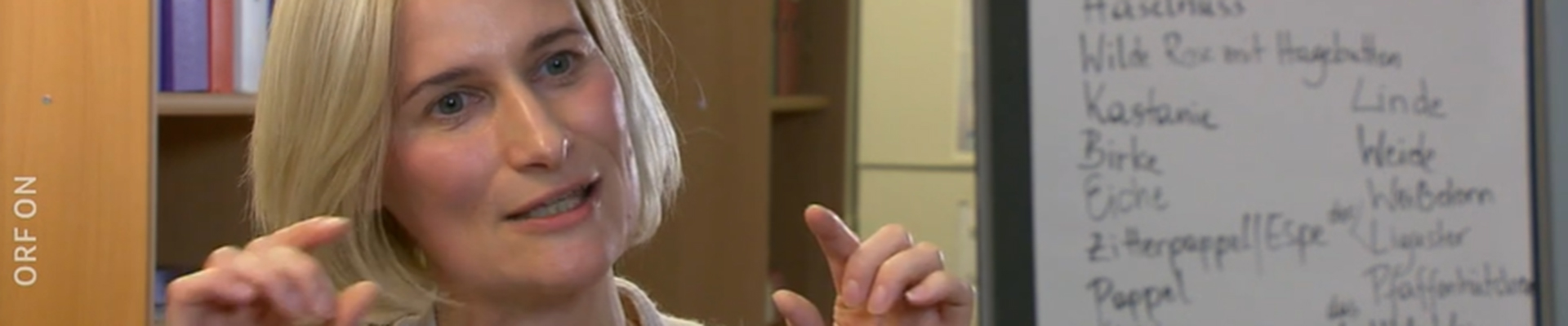 BhW Geschäftsführerin Therese Reinel sitzt in einem Schulungsraum vor einem Bücherregal und Flipchart und wird interviewt.