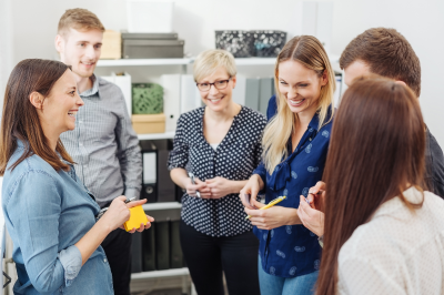 Eine Gruppe junger Erwachsener steht im Kreis. Sie besprechen sich und halten Haftnotizen in den Händen. Die Stimmung ist positiv.