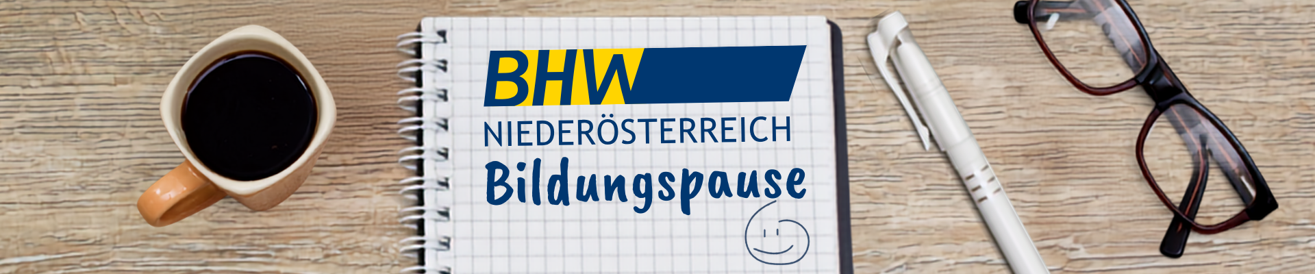 Das Bild zeigt einen Schreibtisch von oben. Darauf liegen ein Block und eine Brille, daneben steht eine Kaffeetasse.
