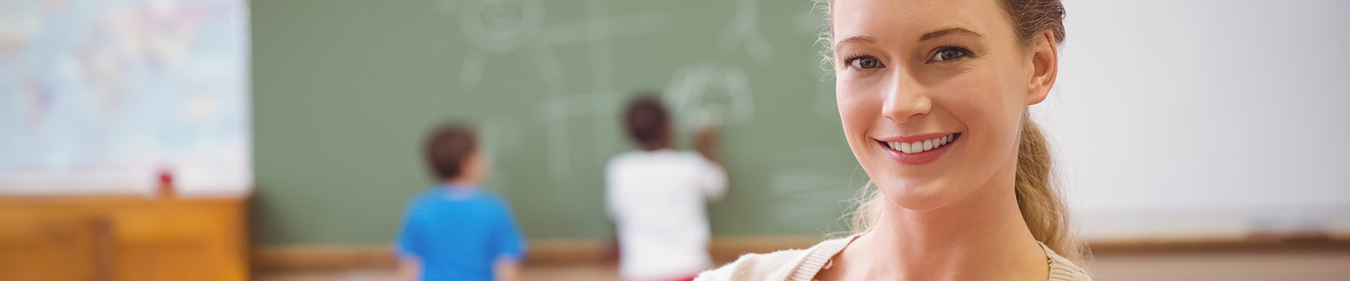 Junge Lehrerin lächelt in die Kamera, im Hintergrund sieht man ihren Klassenraum.