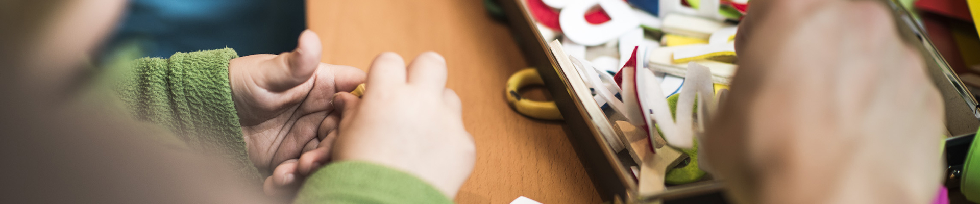 Nahaufnahme von Kinder- und Erwachsnenehänden die in einer Schachtel mit Spielzeug-Buchstaben wühlen.